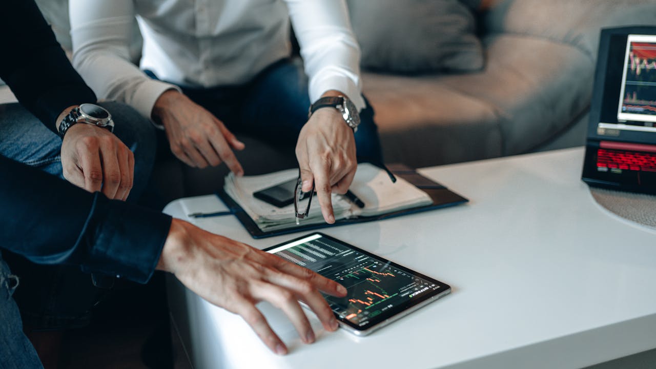 Two businessmen using a tablet to analyze financial data indoors.